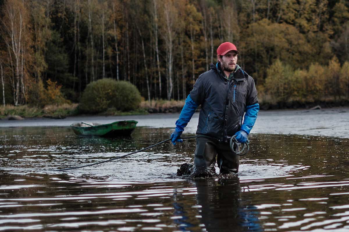 Biofisch Mitarbeiter mit roter Cap beim Abfischen im Teich